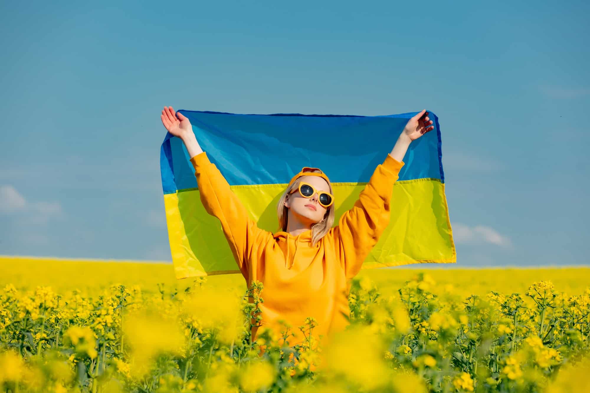 Woman in yellow hoodie and ukrainian flag in rapeseed field